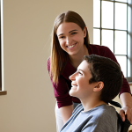 Passion and Empathy in Action**

Prompt: A warm, brightly lit scene in a modern rehabilitation center. A counselor, with a genuine smile, is actively listening to a young adult in a wheelchair. The counselor is leaning slightly forward, maintaining eye contact, and taking notes. The young adult is gesturing with their hands while speaking, their face showing a mix of determination and hope. Soft, natural light streams in from a nearby window. The overall impression is one of connection, trust, and genuine care. Include adaptive technology subtly in the background, like a tablet with accessibility features. Focus on the human connection and positive interaction.
**